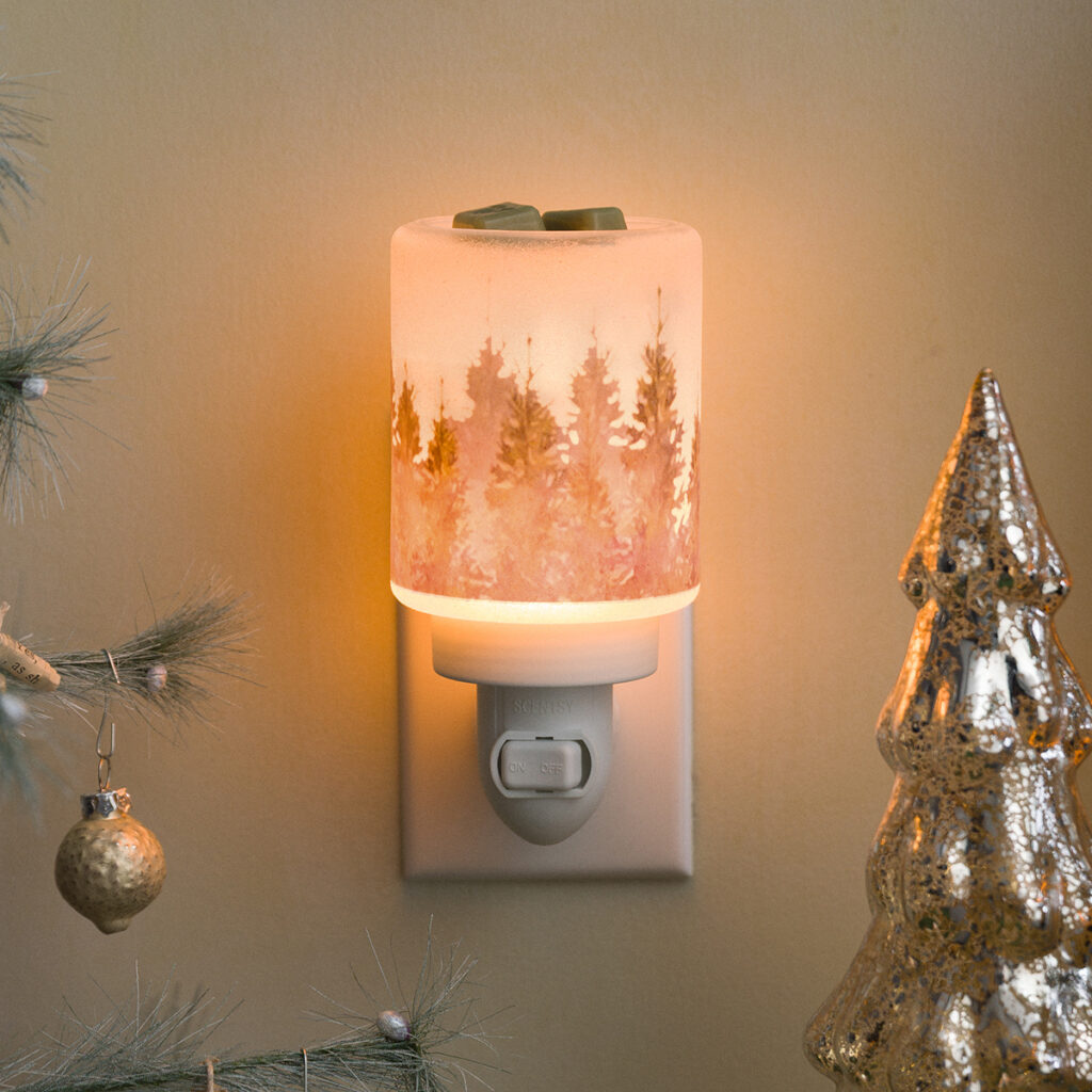 The Evergreen Pine Mini Warmer by Scentsy glowing with a soft golden light, surrounded by simple holiday decor — a gold Christmas tree and frosted greenery. The pine forest design gives off peaceful, cozy cabin vibes, perfect for winter home styling and Christmas decorating.