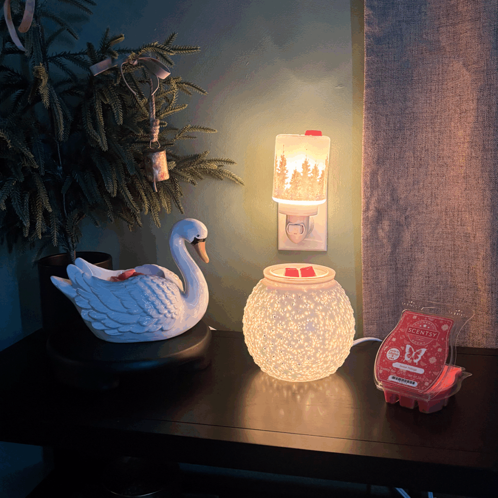 Evening glow vibes ✨ My All Is Calm Mini Warmer, swan warmer, and hobnail warmer are all melting cozy red Scentsy wax bars — total winter mood. Soft light, warm scent, and the prettiest little setup with my mini tree and rustic bells. Cozy home goals for the holiday season.