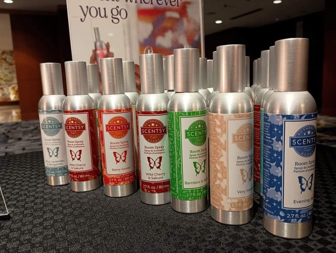 Table display of Scentsy Room Sprays in multiple fragrances including Wild Cherry & Sakura, Berry Sweet, Bamboo & Rain, and Evening Sky. Travel-friendly air fresheners for instant scent anywhere