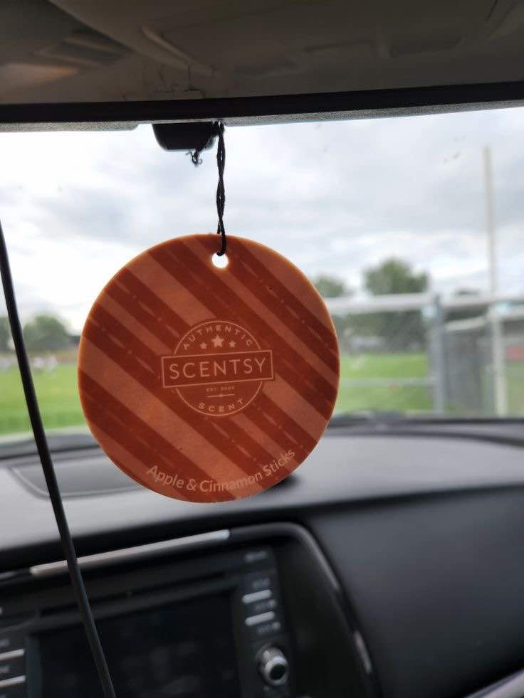 Scentsy Scent Circle in Apple & Cinnamon Sticks hanging from a car rearview mirror, filling the car with warm fragrance. Easy and affordable way to keep your car smelling amazing