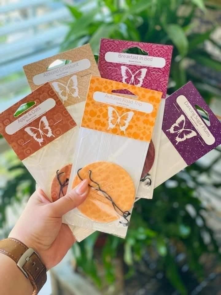 Hand holding colorful Scentsy Scent Circles in their packaging, featuring Autumn Road trip and other fragrances. These long-lasting air fresheners are perfect for cars, closets, and small spaces