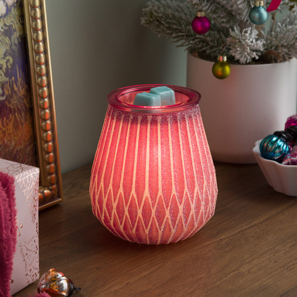 The Frosted In Fuchsia by Scentsy glowing in soft pink with icy glitter detail, styled on a cozy holiday table with mini Christmas ornaments and warm festive decor. Total merry-and-bright vibes for winter home fragrance.