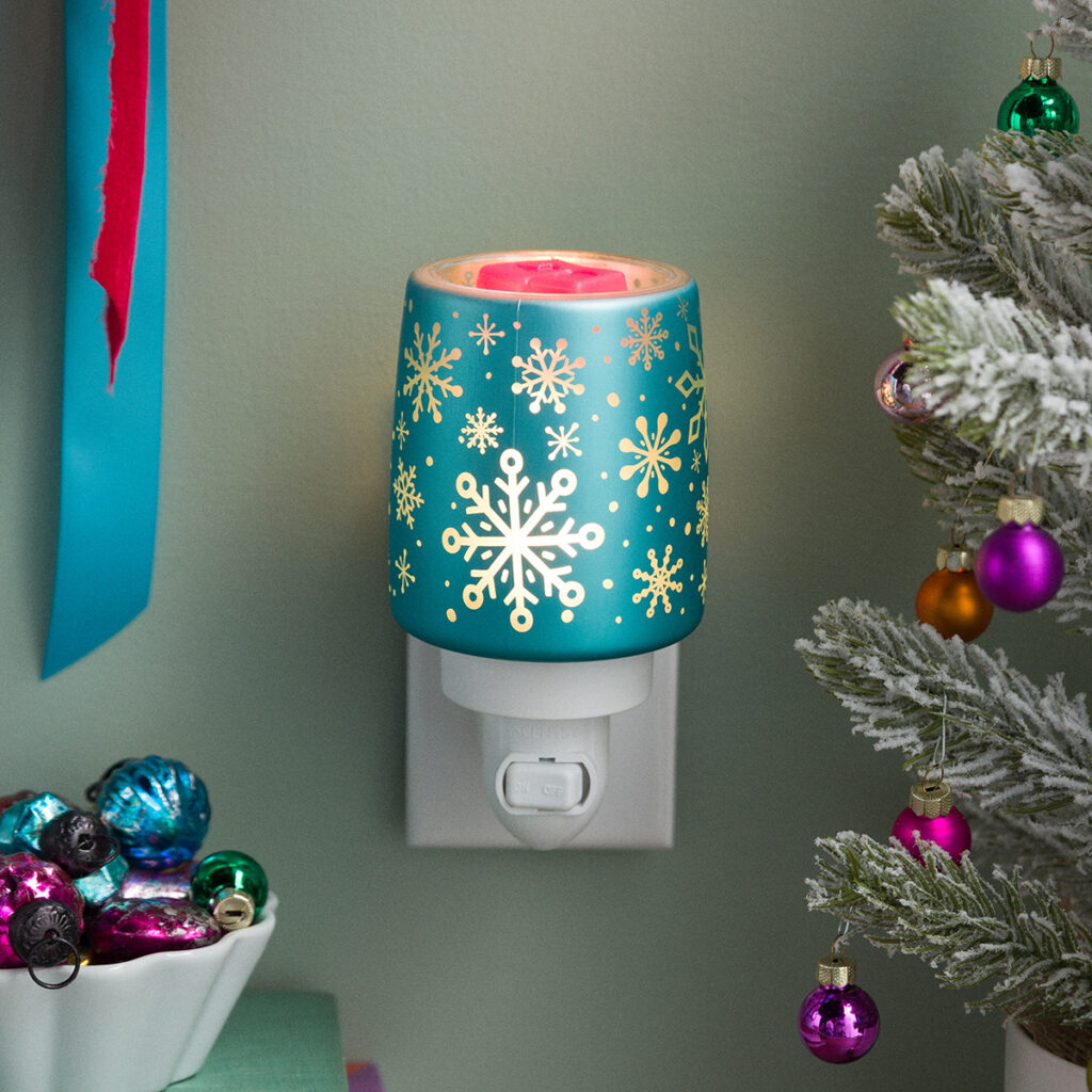 The Frostique Mini Warmer by Scentsy lit up with glowing snowflakes — a fun pop of teal for your Christmas decor. Brings cozy winter light and the scent of the season to any space.
