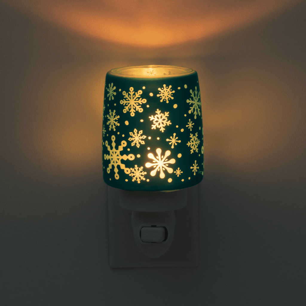 The Frostique Mini Warmer by Scentsy glowing in the dark, highlighting its cutout snowflakes. Perfect for creating soft winter light and festive fragrance.