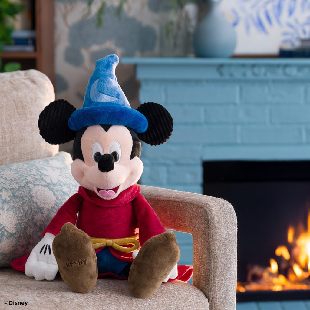 Disney Sorcerer Mickey Scentsy Buddy displayed on a couch with colorful pillows, wearing his blue hat and red robe from Fantasia.