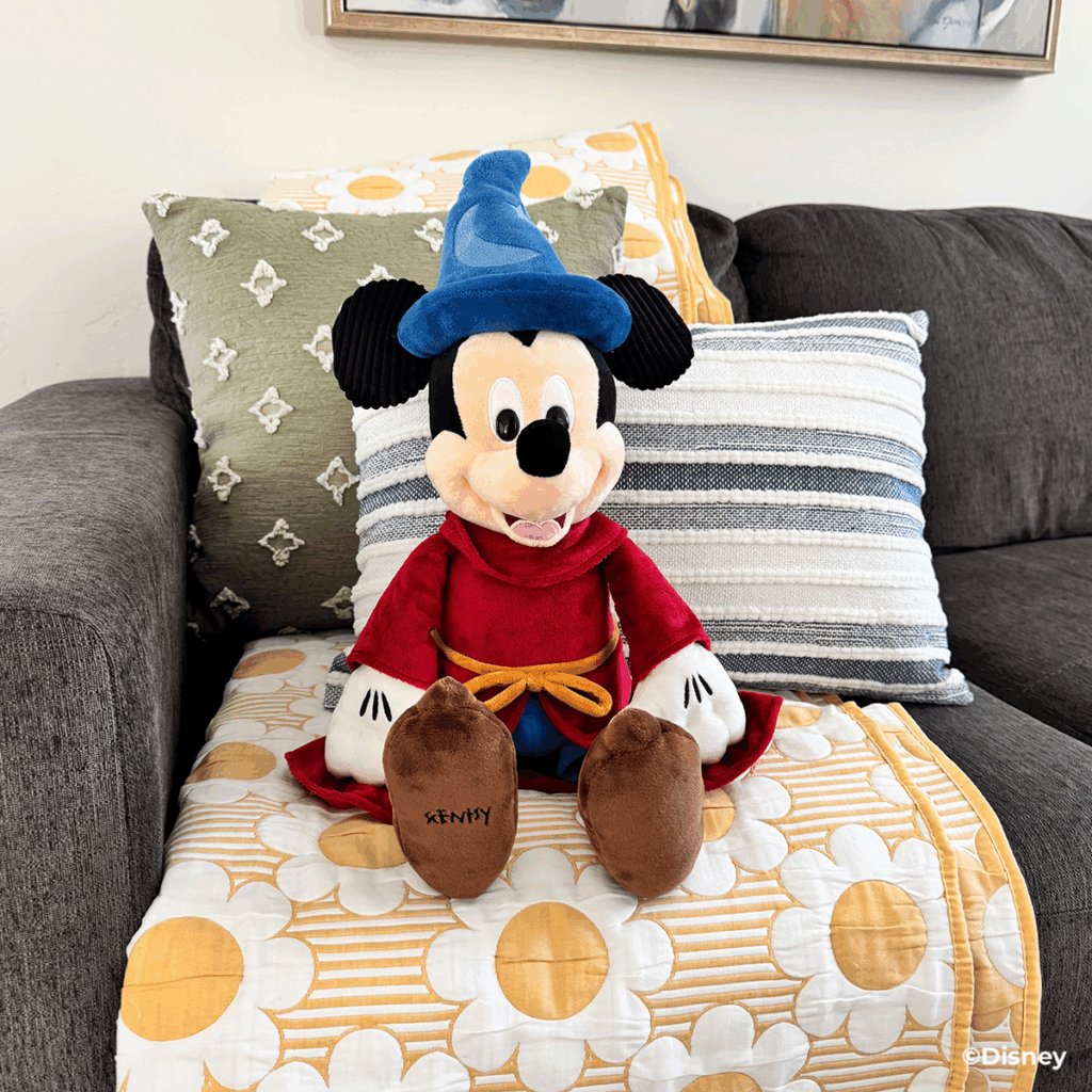Disney Fantasia Sorcerer Mickey Scentsy Buddy sitting on a chair by a cozy fireplace, wearing his signature red robe and blue sorcerer hat.