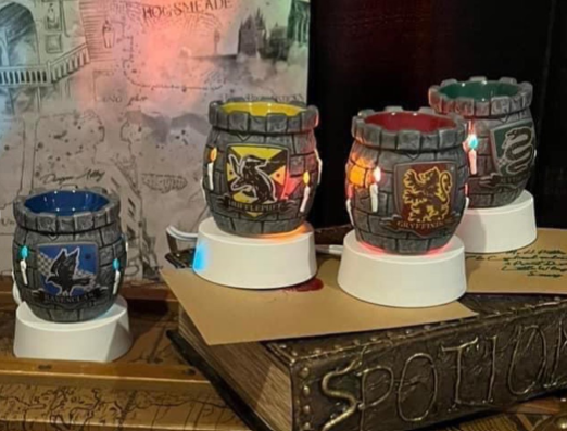 Harry Potter Scentsy mini warmers representing all four Hogwarts houses — Gryffindor, Hufflepuff, Ravenclaw, and Slytherin — displayed with glowing details and Hogwarts map background.