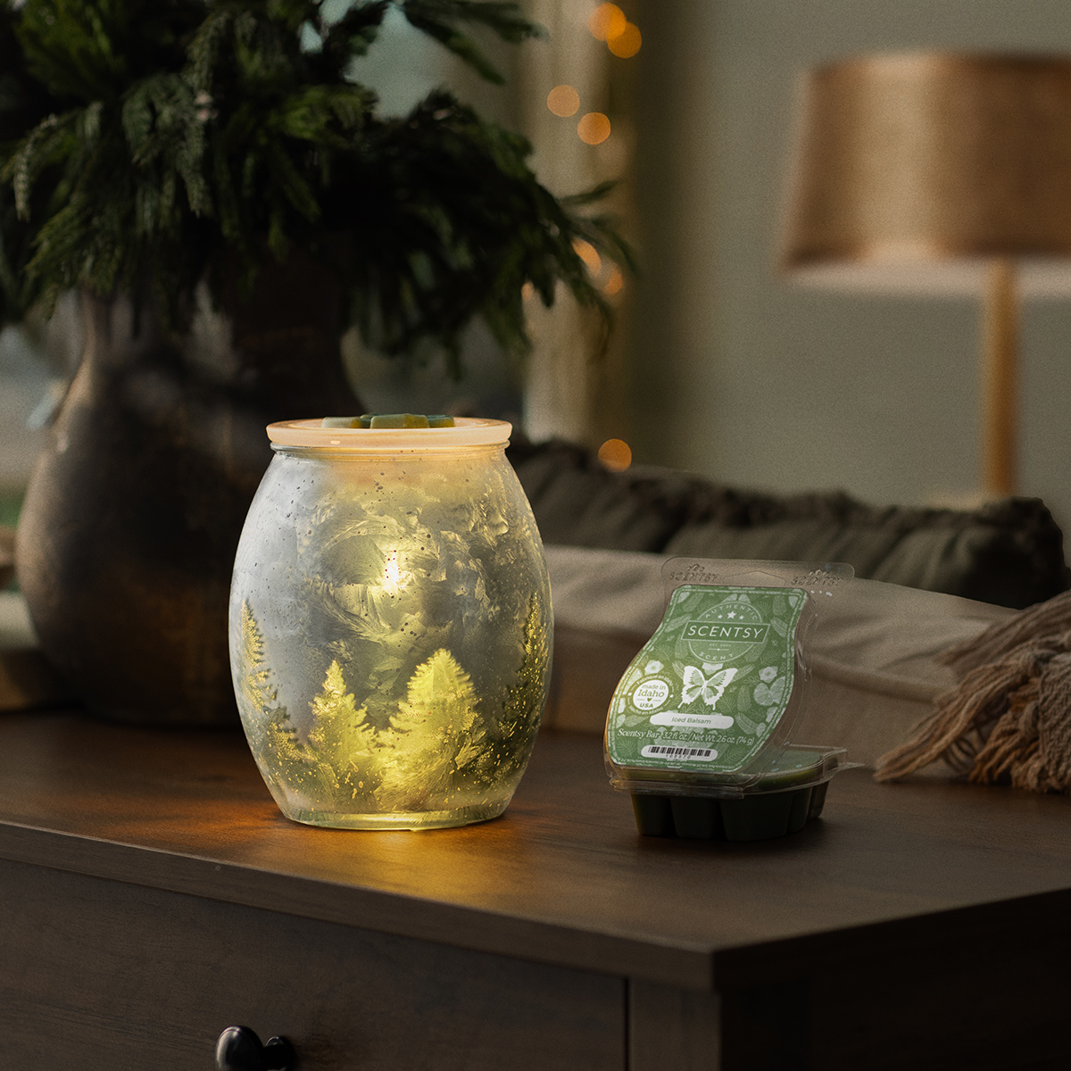 Scentsy Wintercrest Warmer glowing on a wooden side table beside a green wax bar, holiday décor in the background.