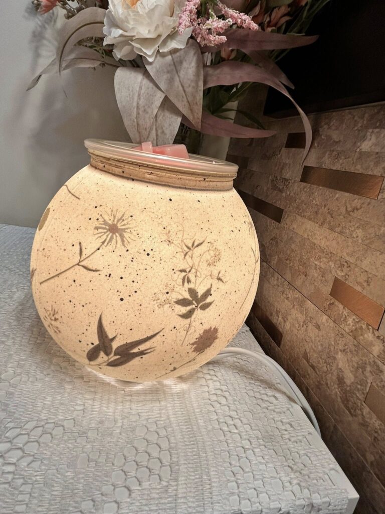 Veiled Meadow warmer on a white table cloth with a pressed flower in stone look
