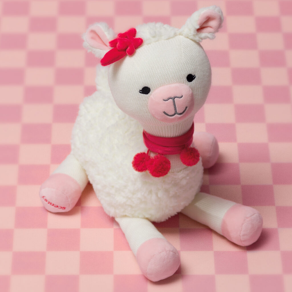 Lalita the Llama Scentsy Buddy plush with pink Valentine’s details on a soft checkered background.