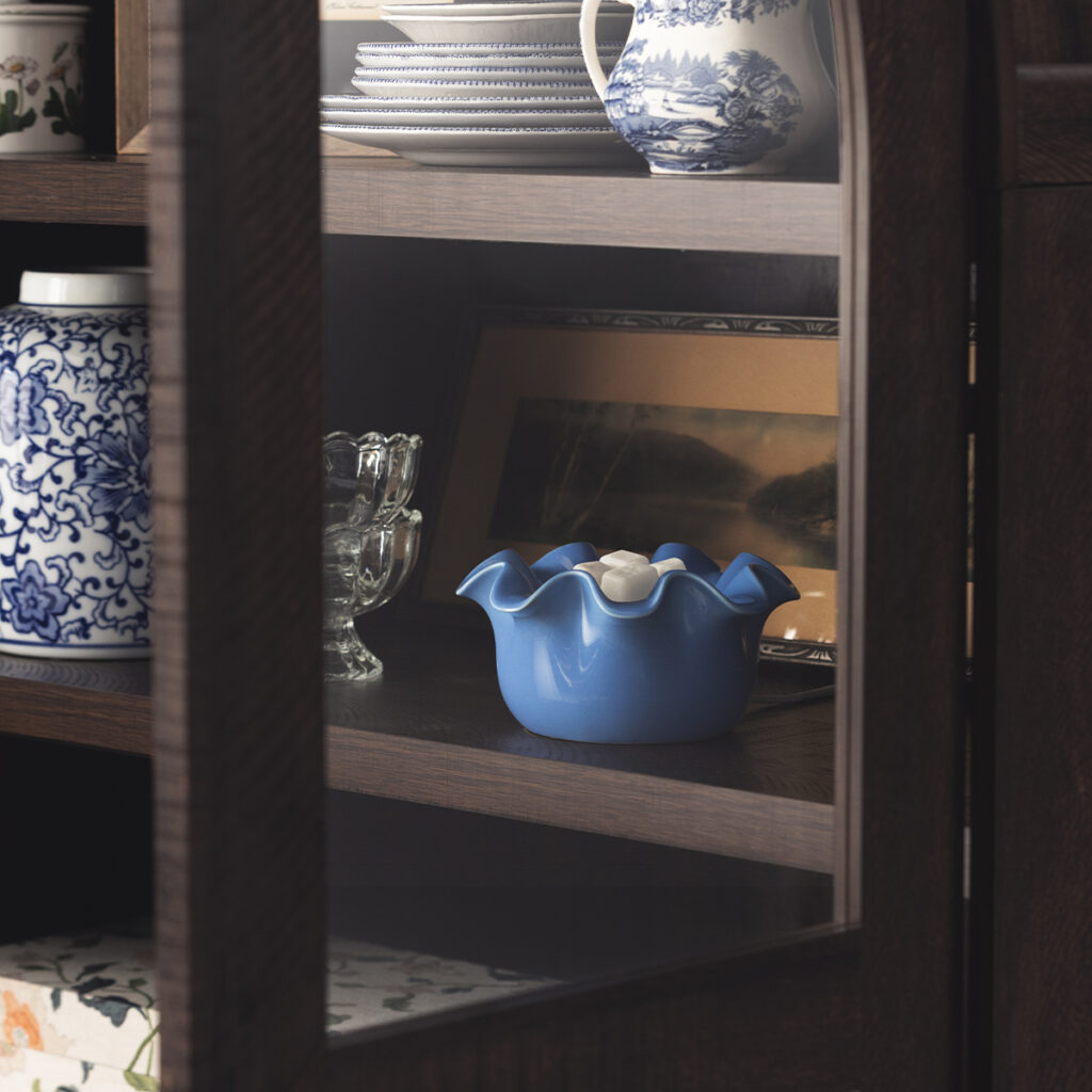 Blue Scentsy Petite Ruffle warmer displayed on a shelf with dishes and framed décor.