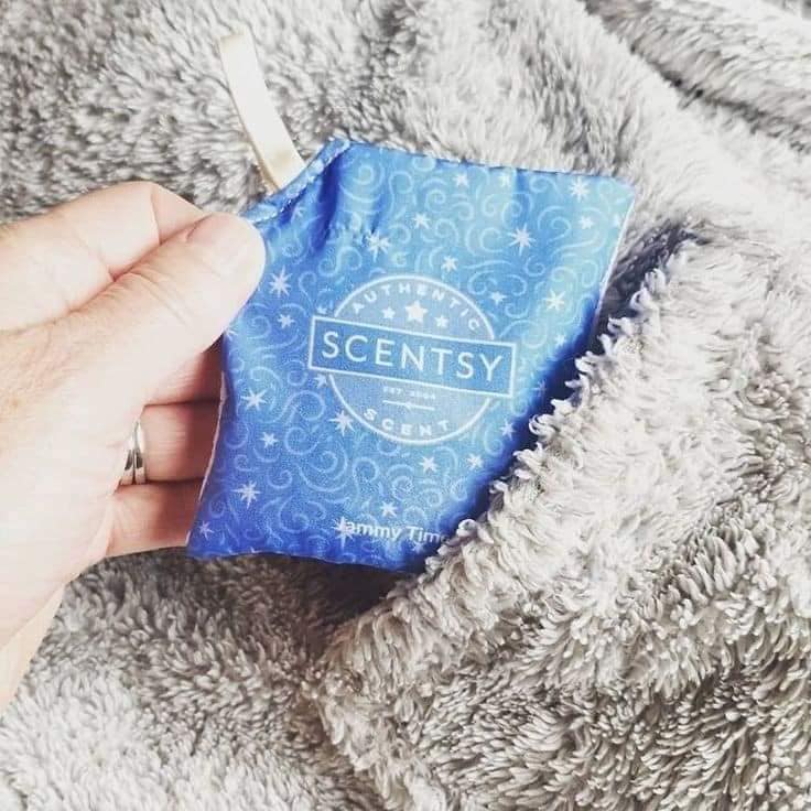 Hand holding a Scentsy Jammy Time scent pak inside a soft blanket, demonstrating how scent paks can keep linens and blankets smelling fresh.