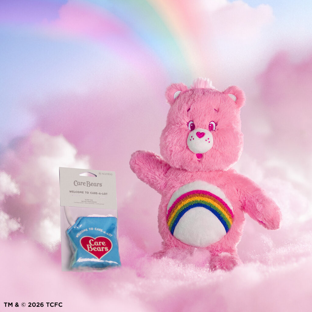 Cheer Bear Scentsy Buddy plush with rainbow belly badge next to the Care Bears Welcome to Care-A-Lot scent pak on a pastel cloud background.