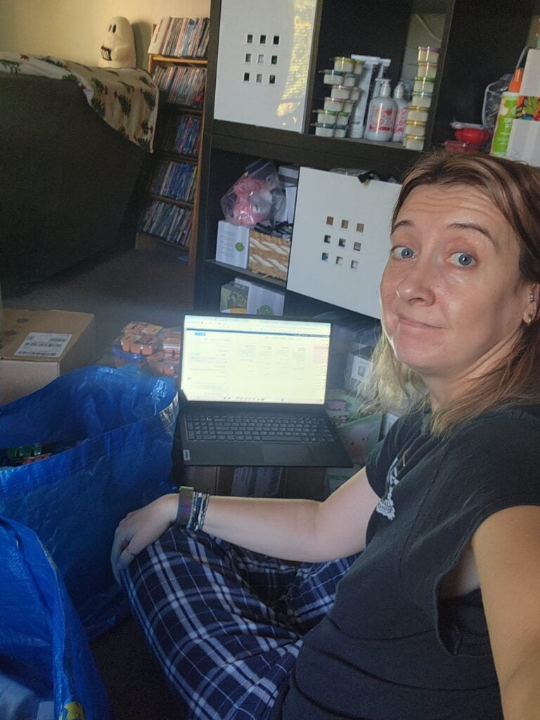 Amber Grillot working from home with a laptop, planner, and shipping supplies while organizing her small business workspace.
