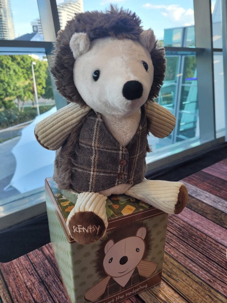 Herbert the Hedgehog Scentsy Buddy wearing a plaid vest and corduroy sleeves while sitting on his collectible box.