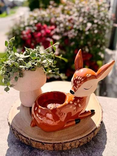 Brown ceramic deer Scentsy Warmer, Restful Doe Scentsy warmer, with white spots resting peacefully beside a small potted plant.