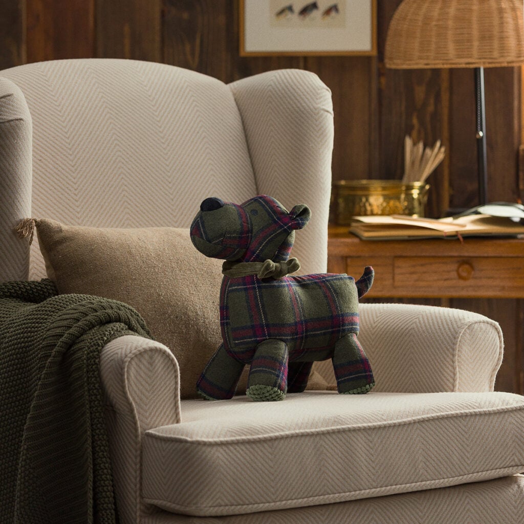 Sutton the Scottie Dog Scentsy Buddy featuring a green and red plaid design sitting on a cozy chair as part of the August 2026 Cozy Cabin Scentsy Edit.