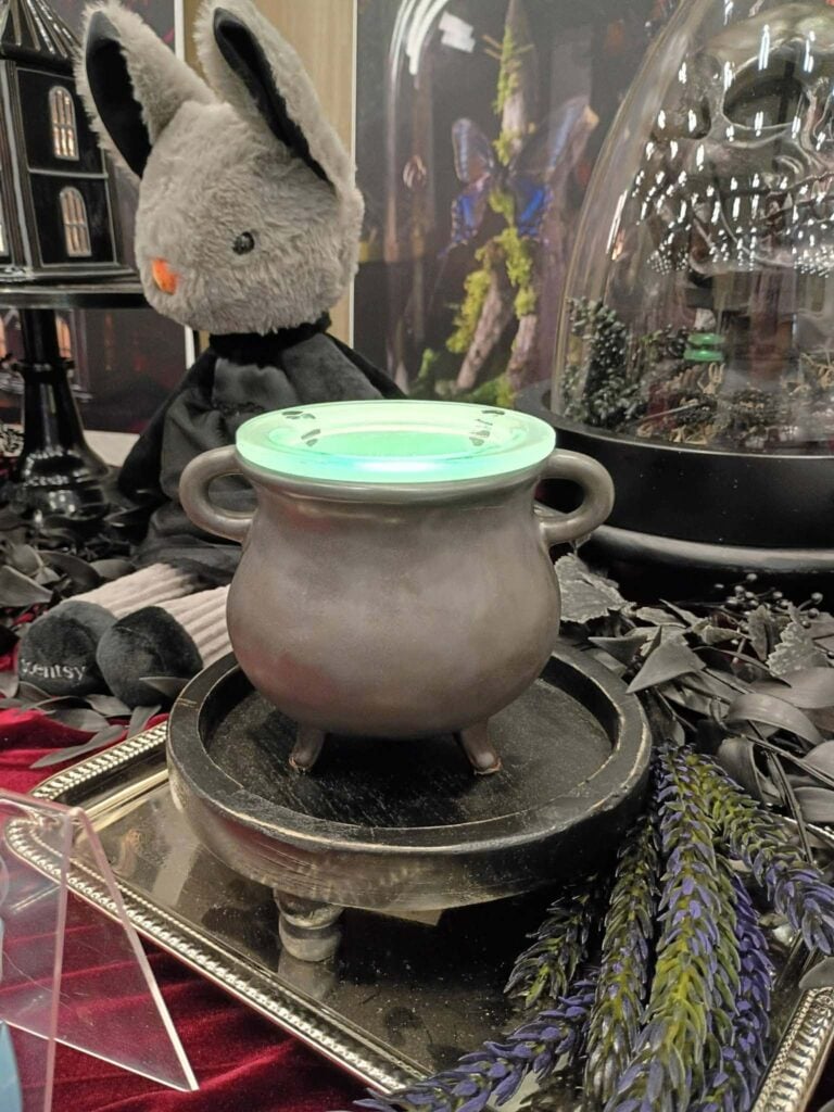 Hocus Pocus Scentsy Warmer with glowing green wax displayed in a black cauldron during the Scentsy September Halloween Collection preview.