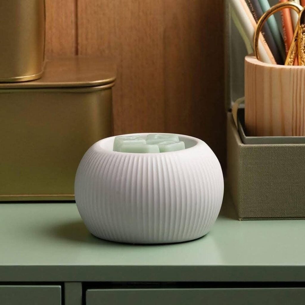White fluted scentsy warmer sitting on a metal green desk with 4 cubes of wax in it
