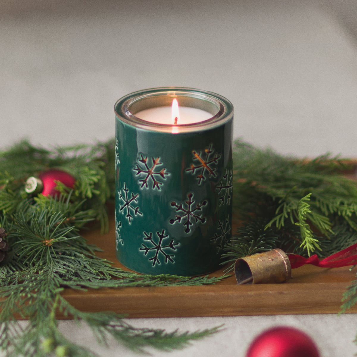 Scentsy Alpine Snowflake Candle Holder in dark green with snowflake cutouts, surrounded by holiday greenery.