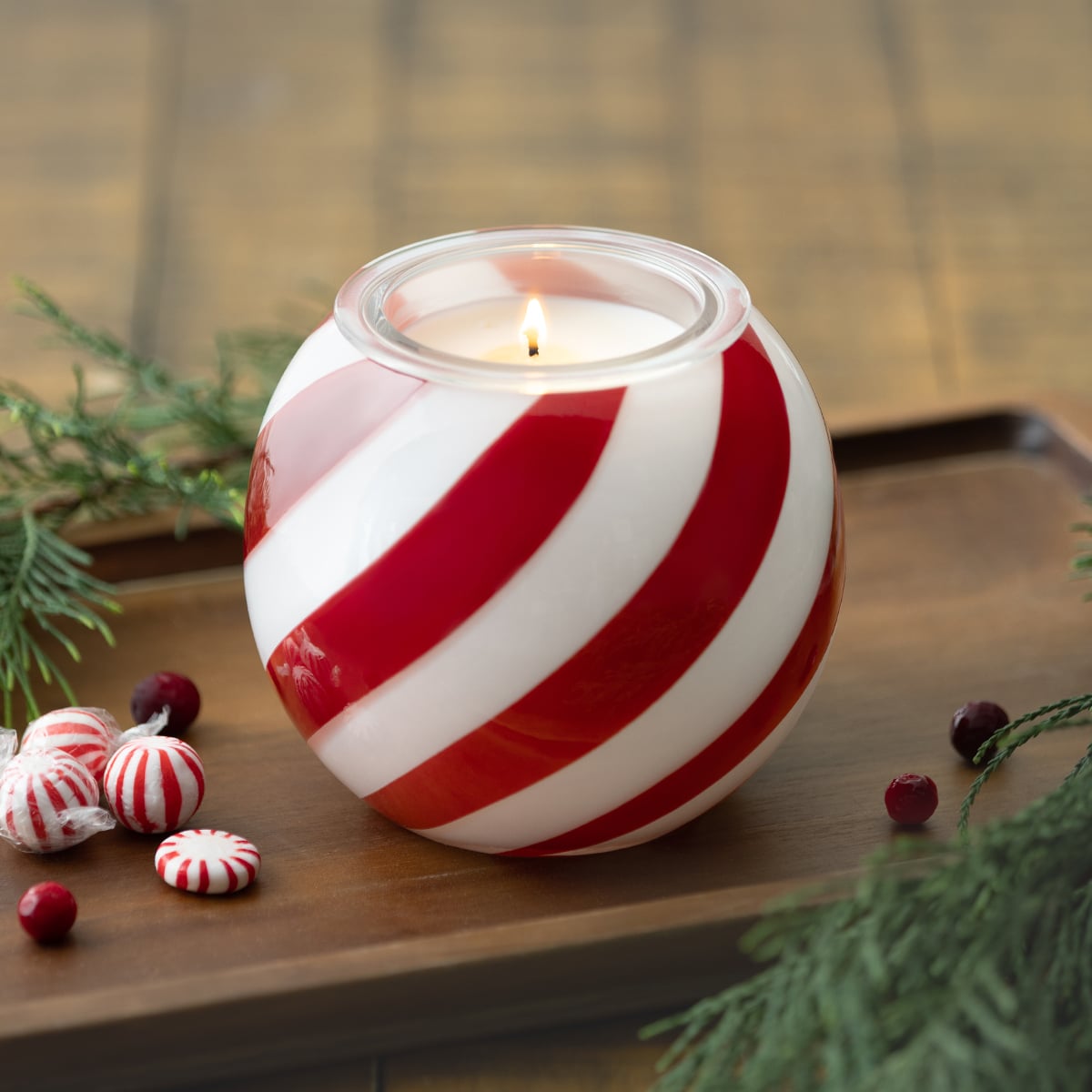 Scentsy Candy Cane Lane Candle Holder with red and white peppermint stripes surrounded by holiday greenery and peppermint candies.