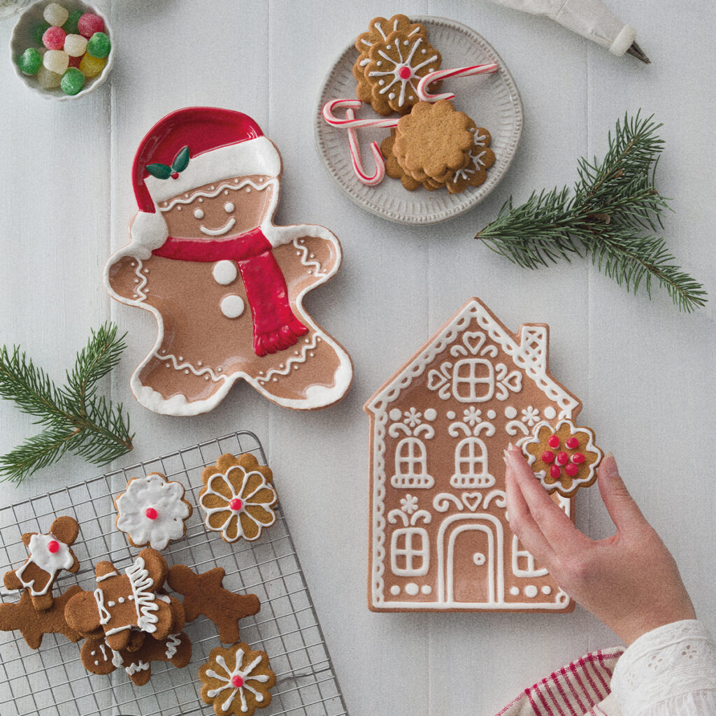 Gingerbread serving plates shaped like a gingerbread man and gingerbread house surrounded by Christmas cookies and candy.