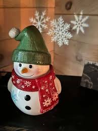Scentsy Looks Like Snow Warmer shaped like a snowman wearing a green hat and red snowflake scarf.