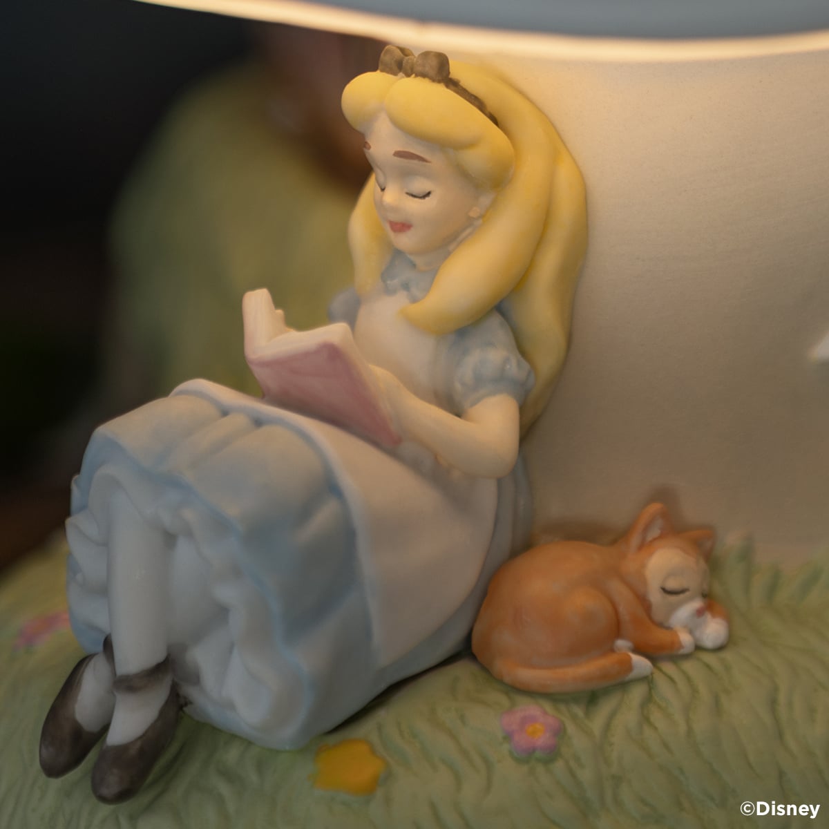 Close-up of Alice reading a pink book beside a sleeping orange cat on the Disney Alice in Wonderland Down the Rabbit Hole Scentsy Warmer.
