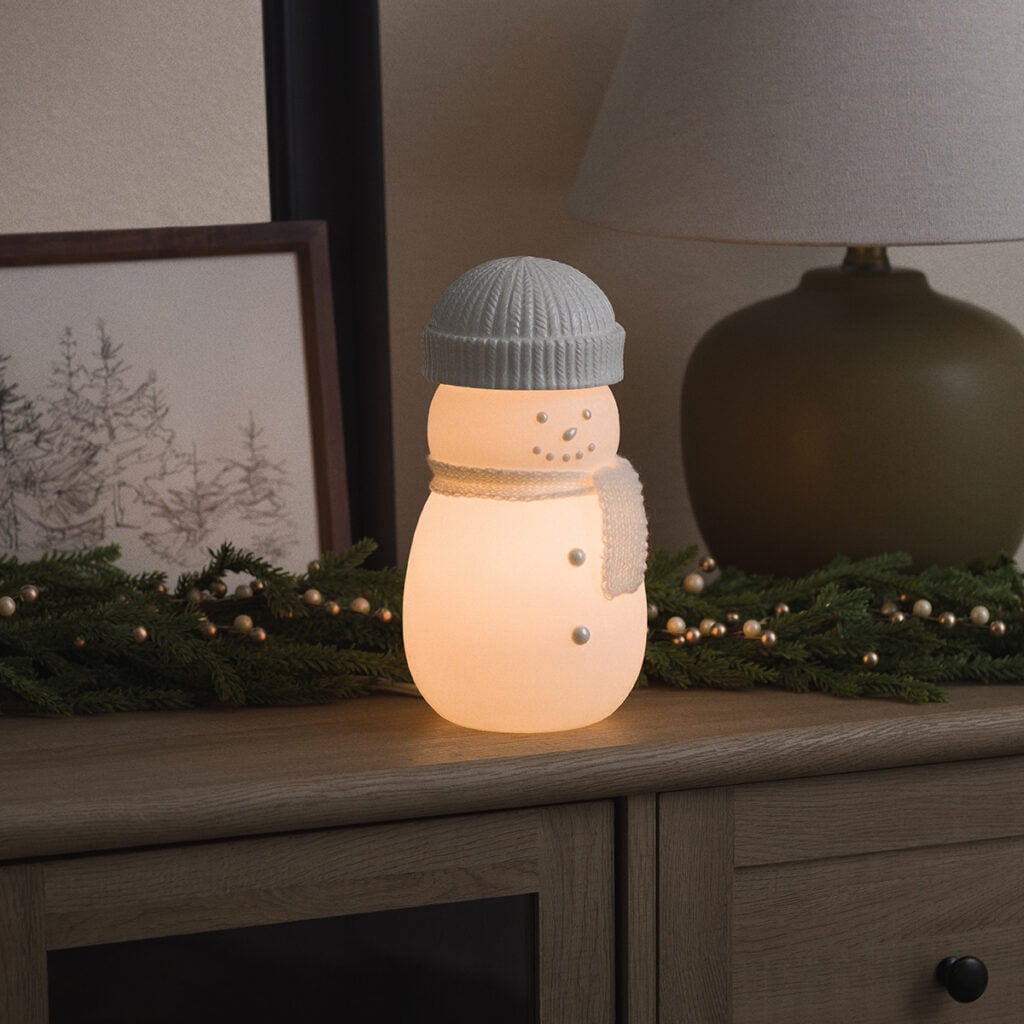 Glowing Frosty Charm Scentsy Warmer shaped like a white snowman wearing a knit hat and scarf, surrounded by winter greenery.